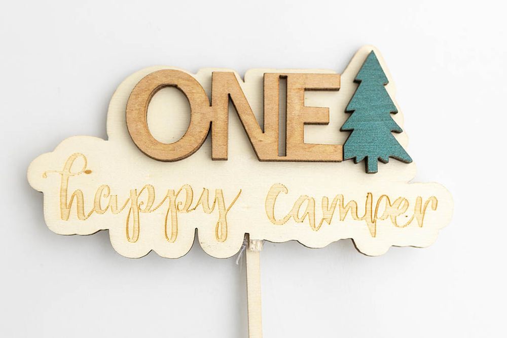 Wooden ONE Happy Camper cake topper with pine tree accent for first birthday party decoration.