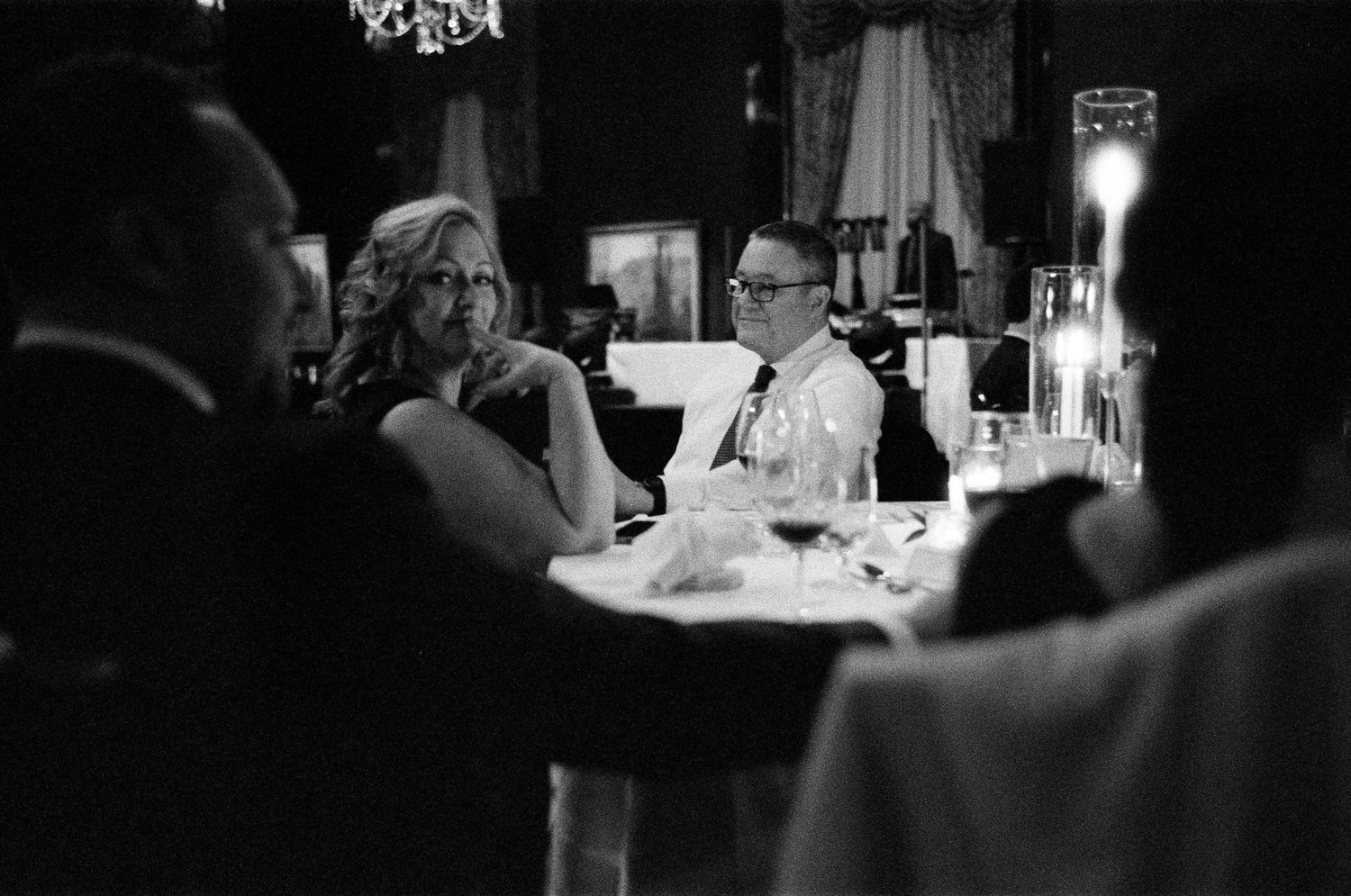 Black and white photo of elegantly dressed guests seated at a candlelit dinner table at a downtown Chicago wedding.