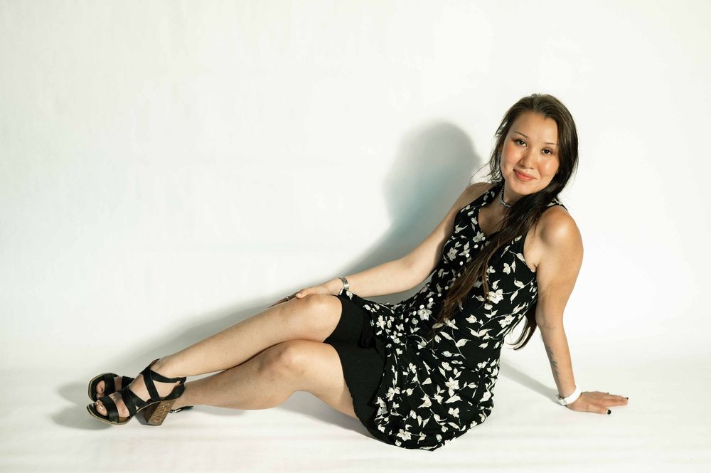 Woman in black floral dress and heels posing on white floor for a professional photo shoot.