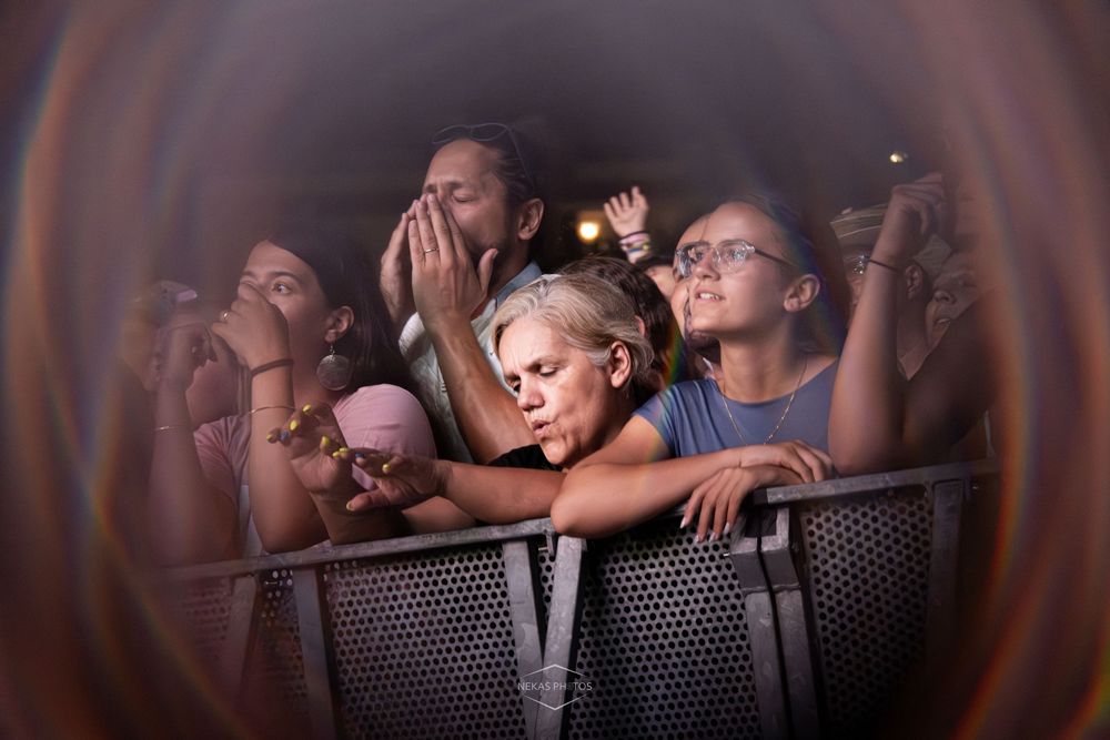 Crowd of concert fans pressed against a metal barrier, captured through a circular vignette lens effect.