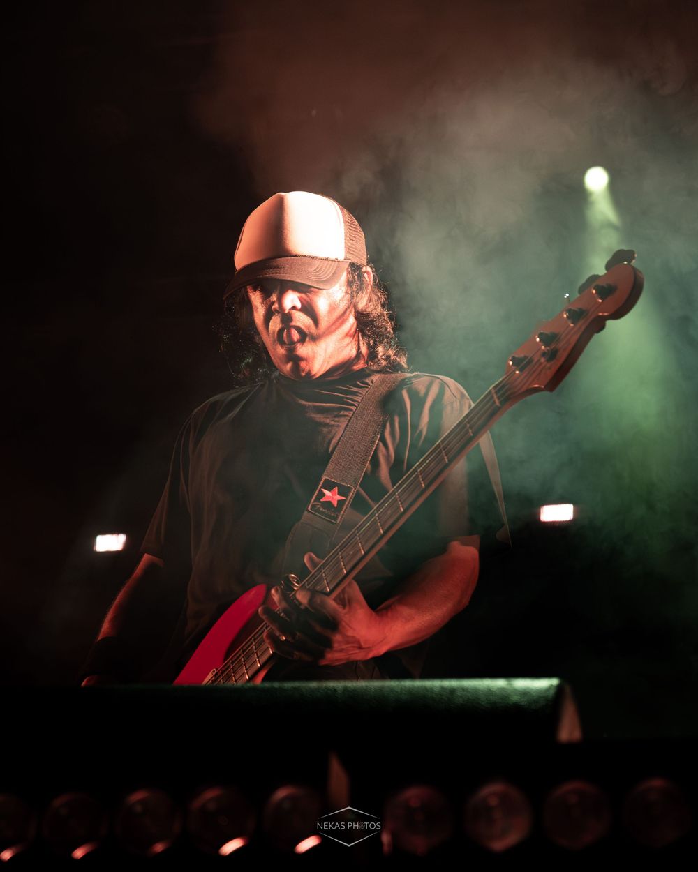 Guitarist performing on stage under dramatic green and white lighting with smoke effects at a live concert.