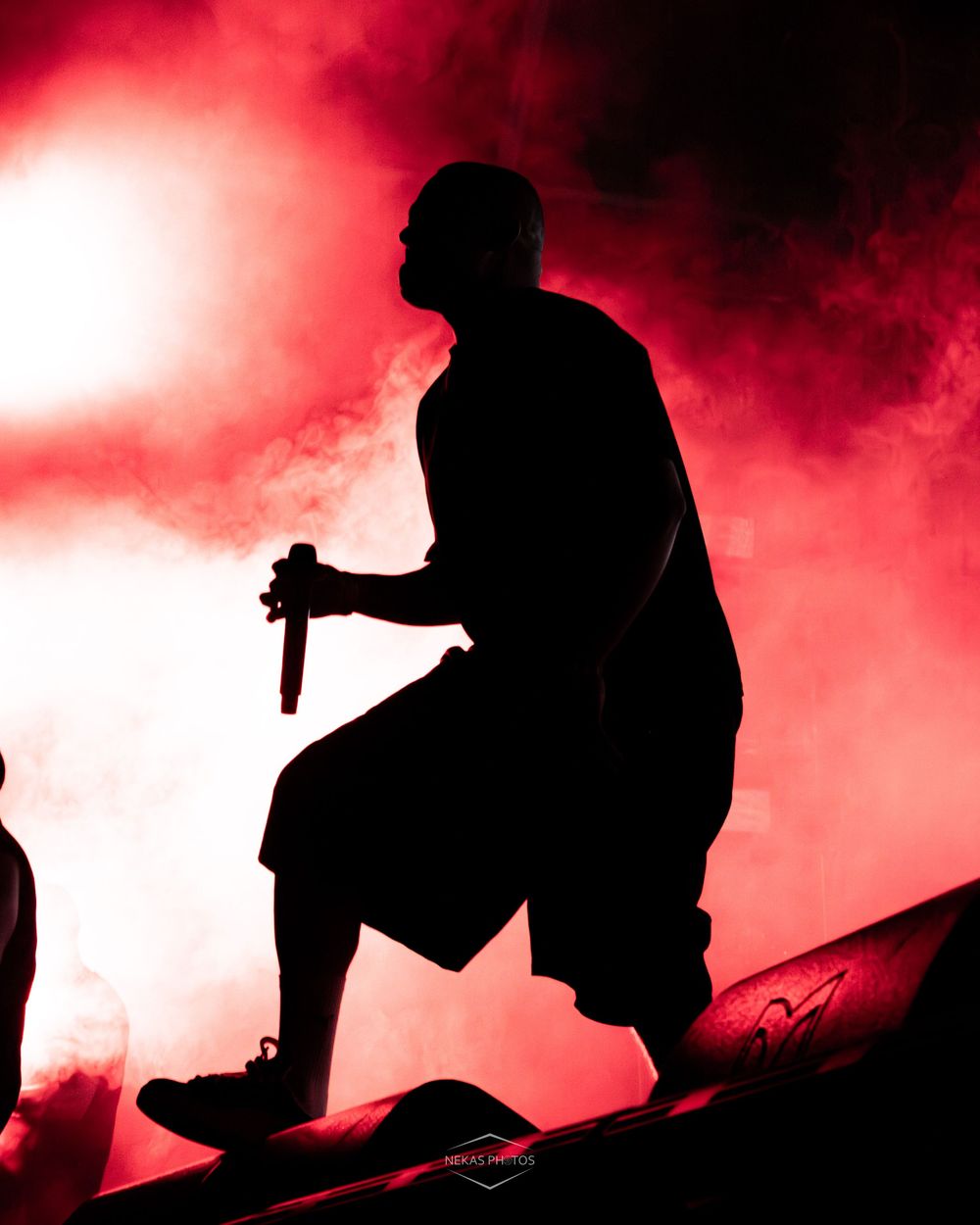 Silhouette of a performer holding a microphone on stage with dramatic red smoky lighting backdrop.