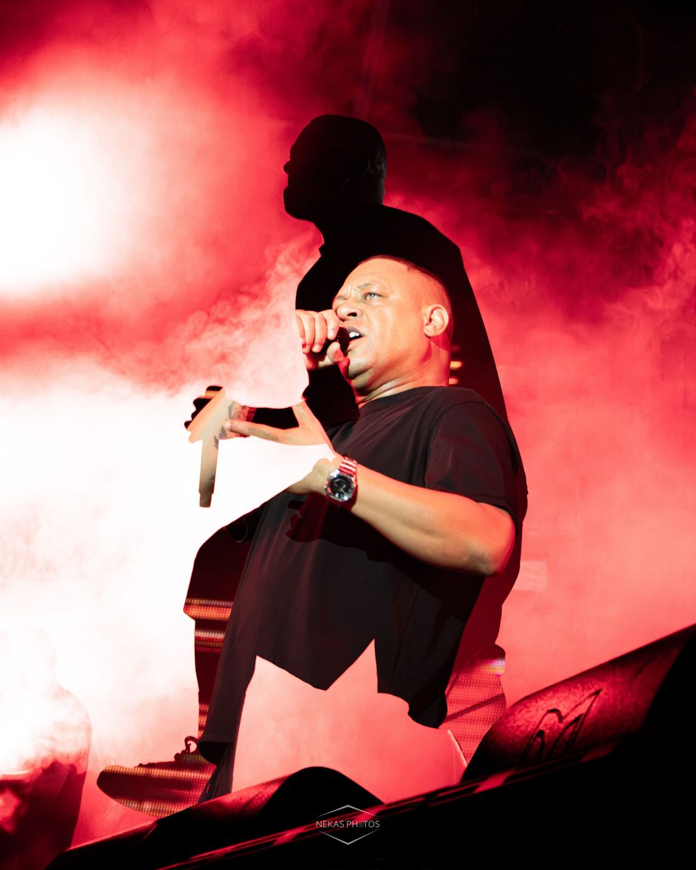 Male performer singing into microphone on stage with dramatic red fog lighting and silhouette backdrop.