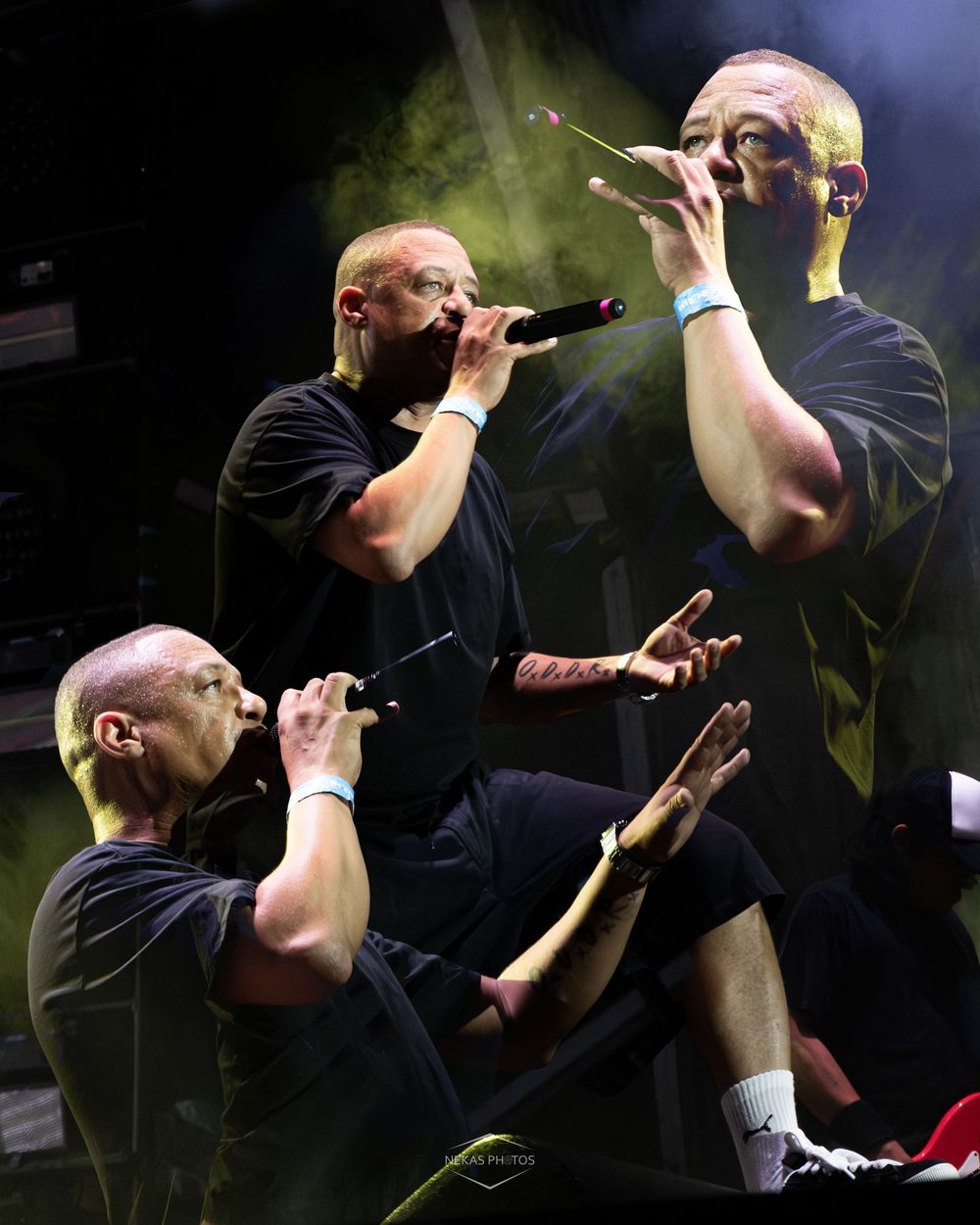 Three performers singing on stage with microphones under dramatic green and white stage lighting.