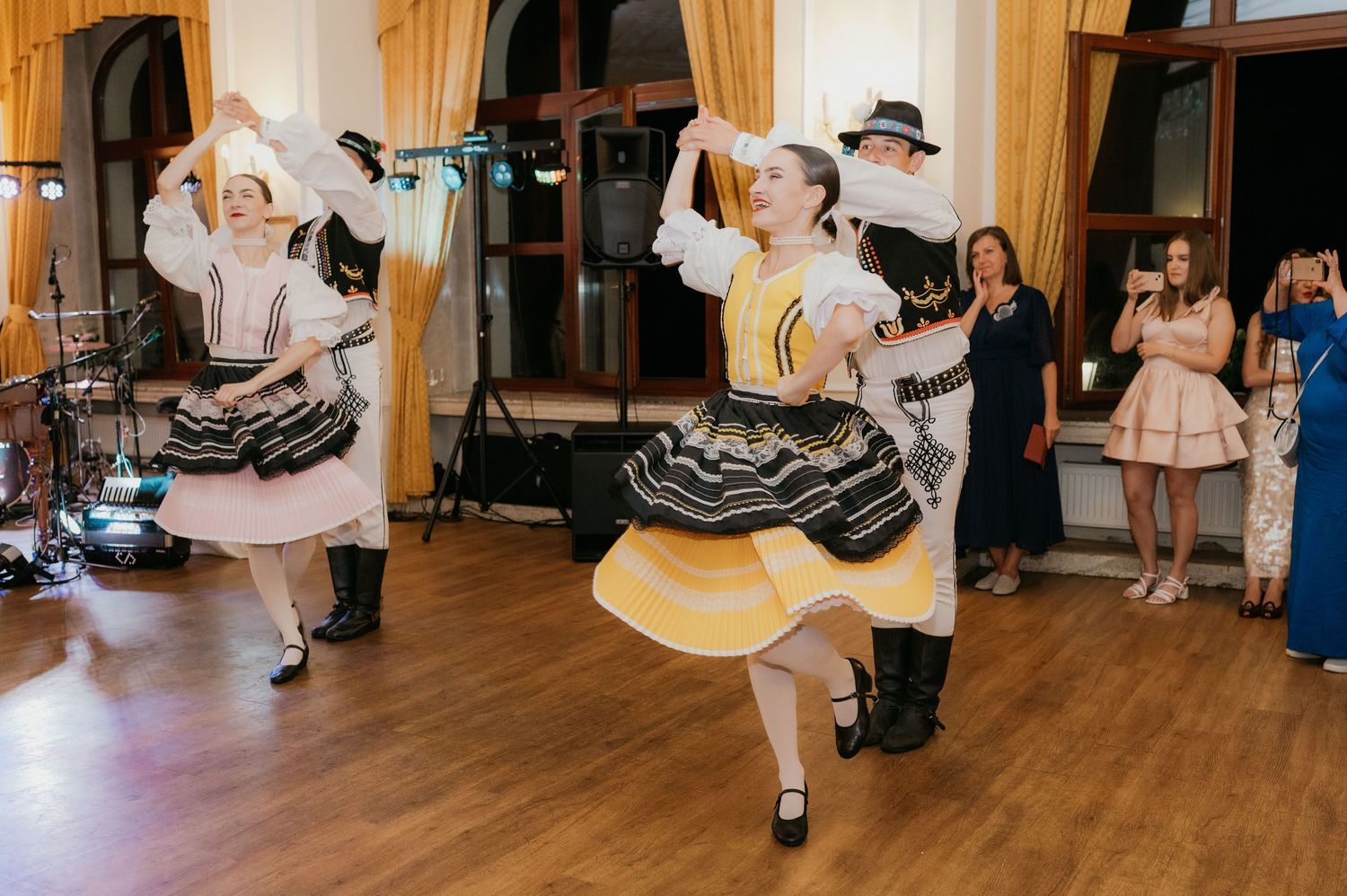 Traditional folk dancers in colorful costumes performing an energetic dance at a wedding reception.