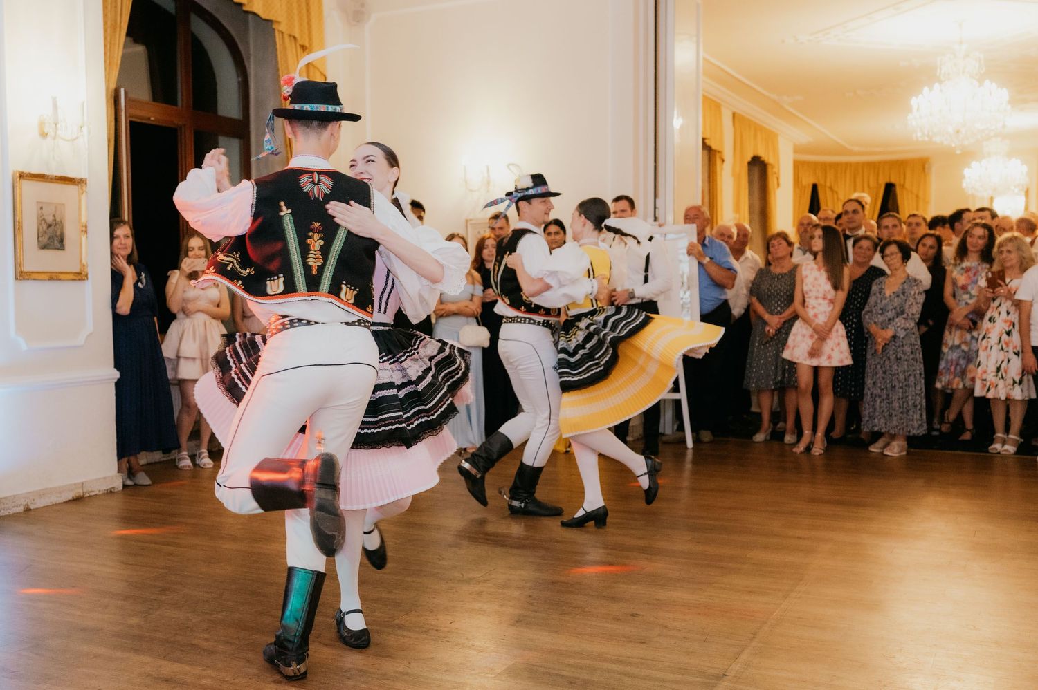 Traditional folk dancers performing in colorful costumes at a wedding reception before guests.