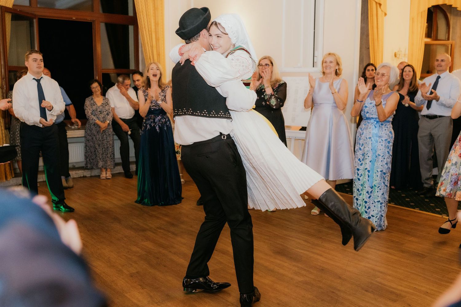 Groom lifting bride during first dance at wedding reception with guests applauding in background.