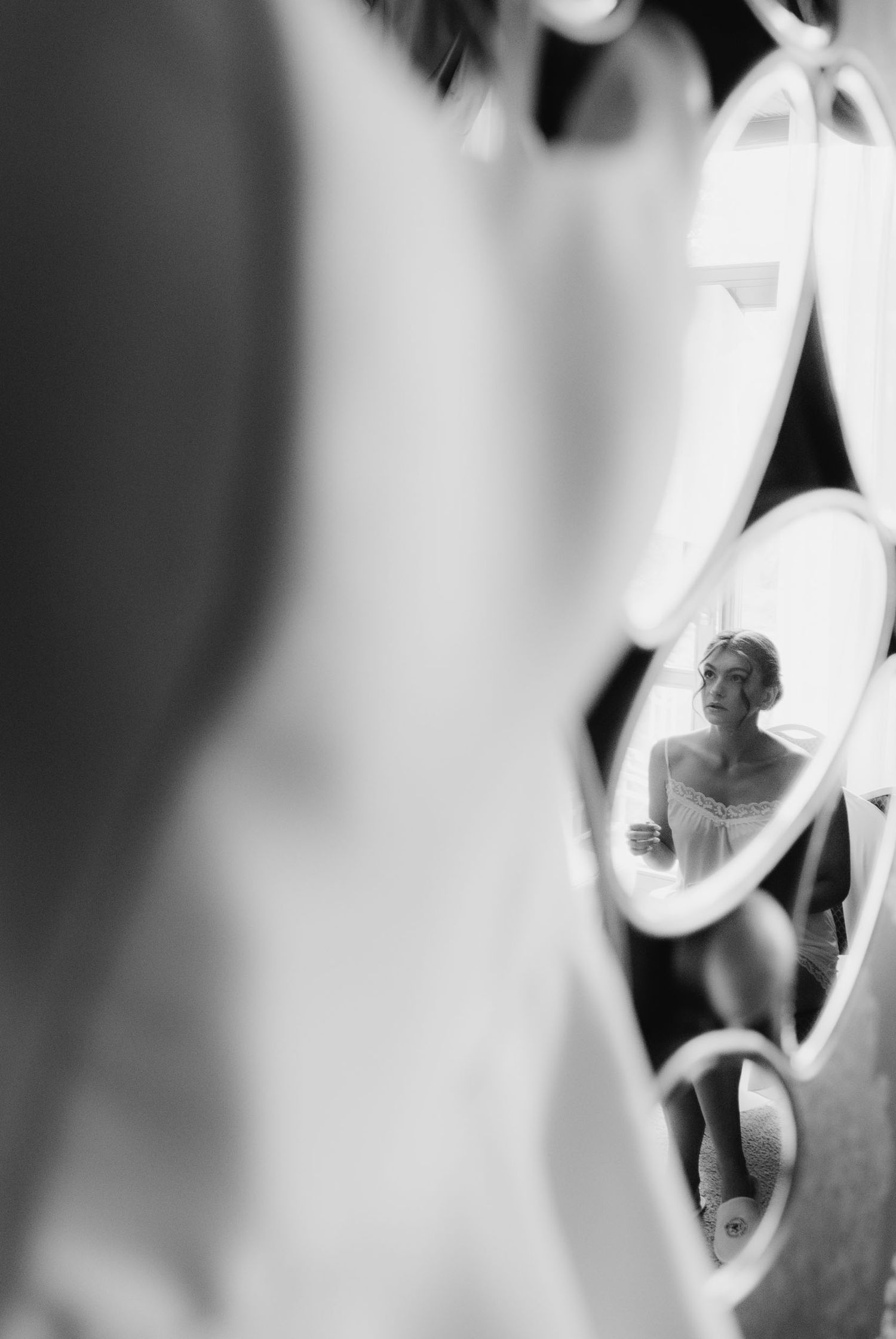 Black and white photo of a bride reflected in heart-shaped mirrors while getting ready on her wedding day.