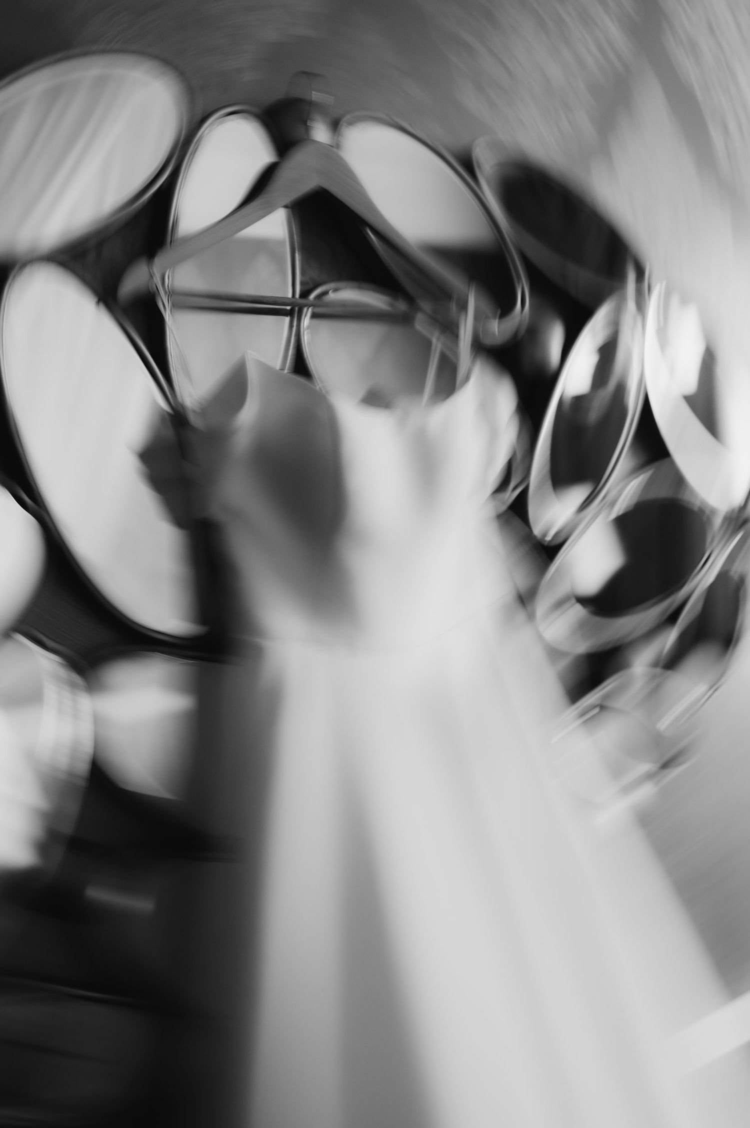 Abstract black and white motion blur photo of a white wedding dress hanging on a rack surrounded by hangers.
