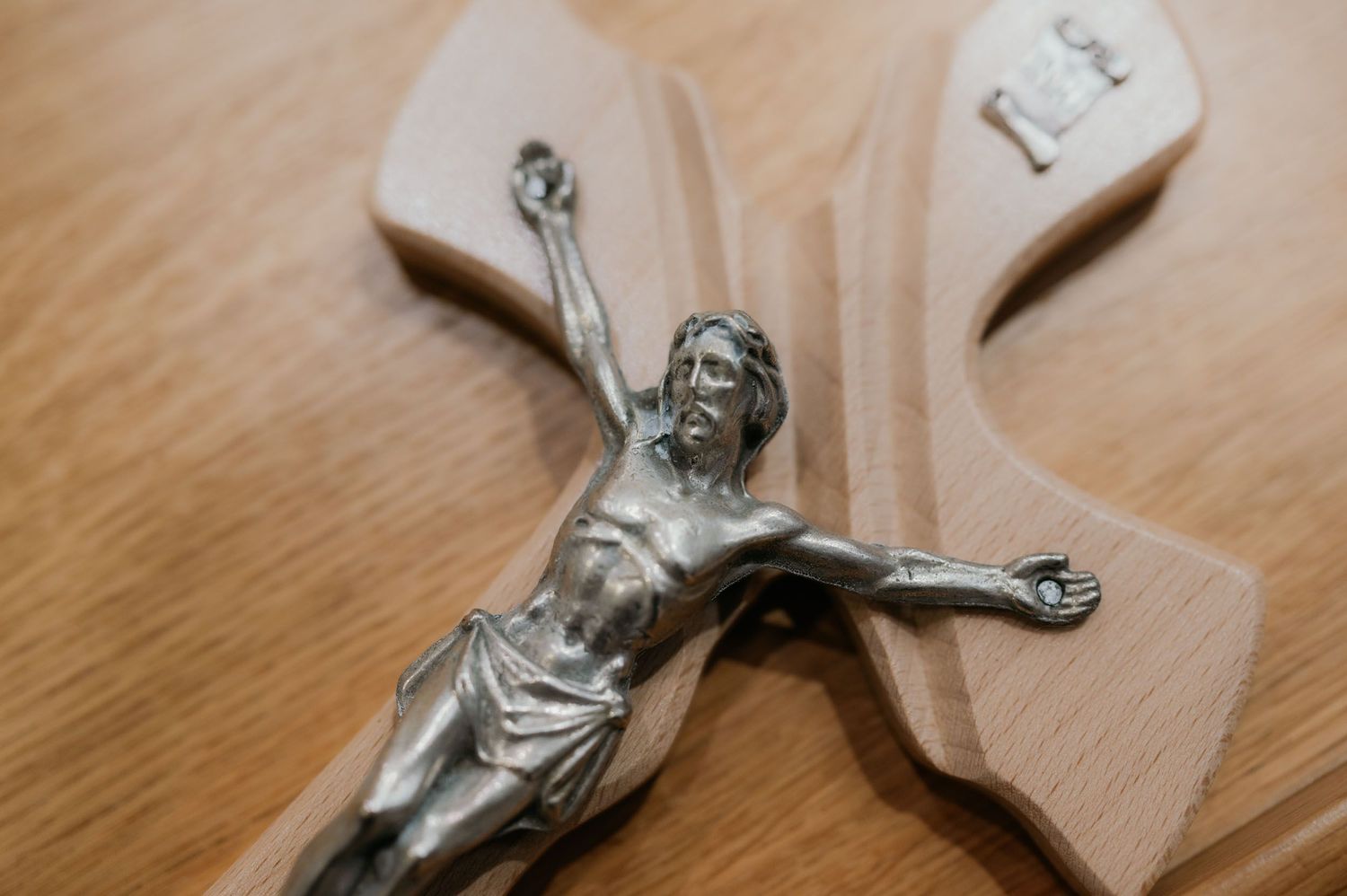 Wooden crucifix with silver metal Jesus Christ figurine on a light wood surface.