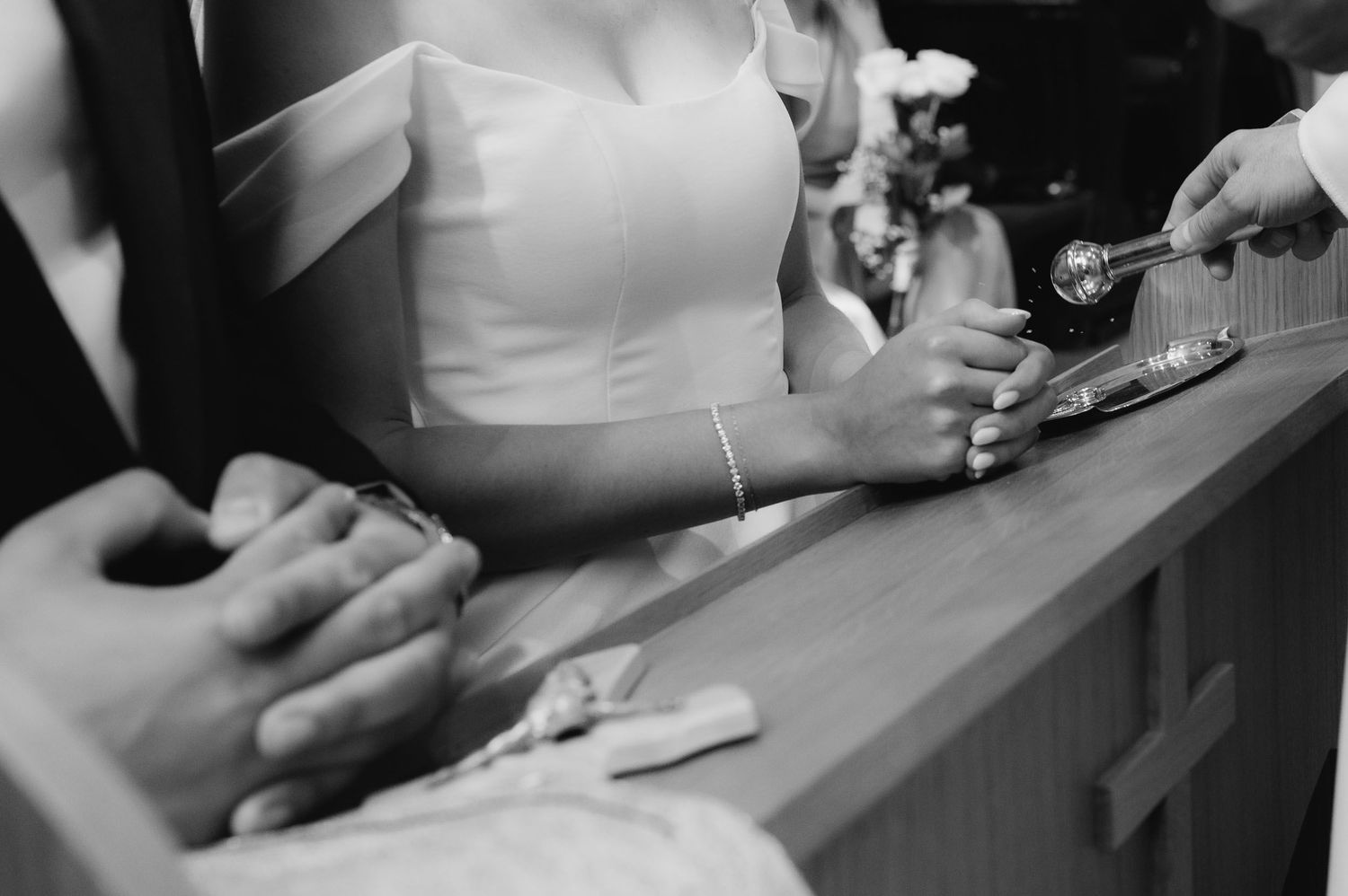 Black and white close-up of bride and groom exchanging rings at church altar.