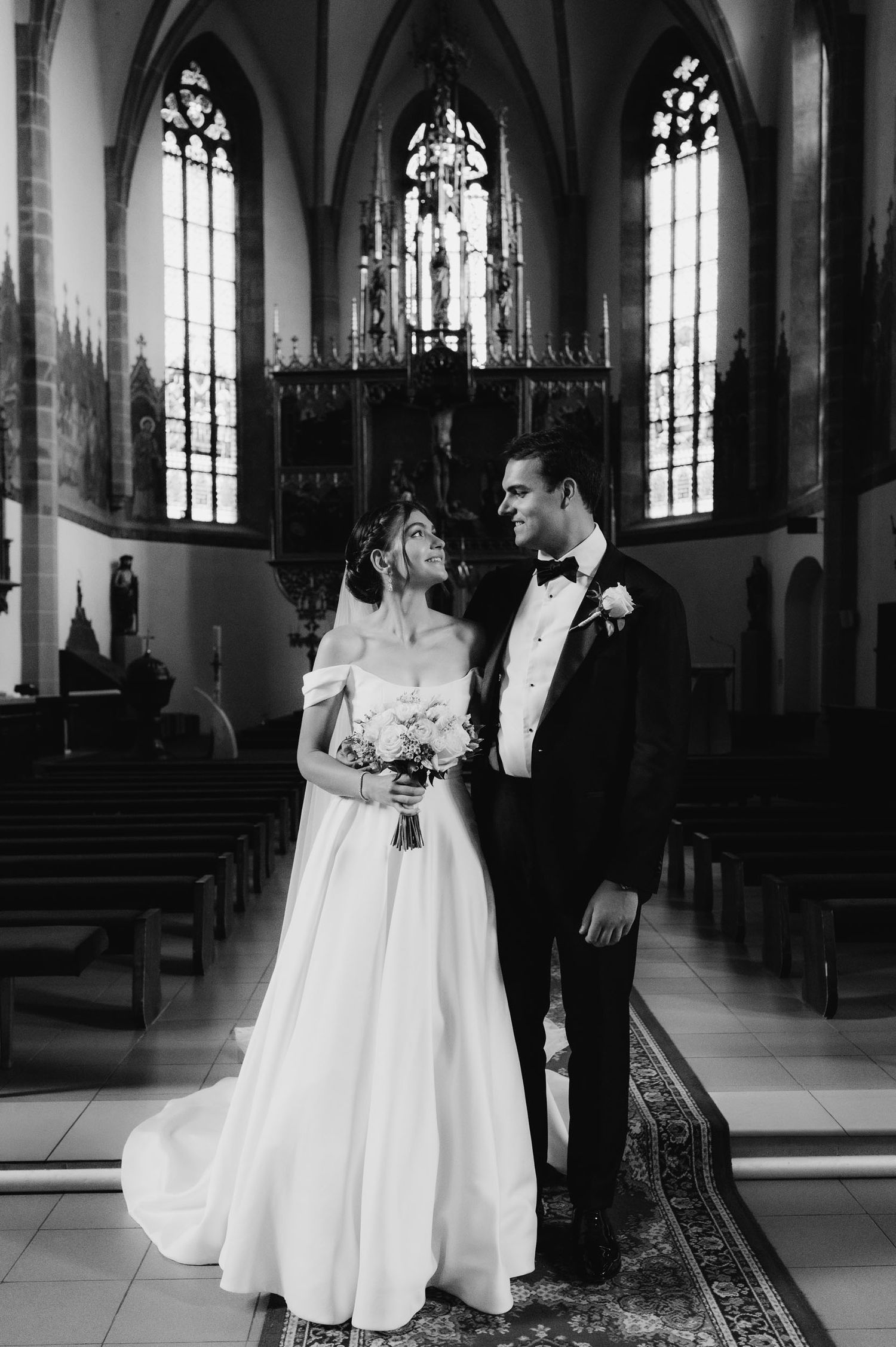 Black and white photo of a bride and groom sharing a romantic moment inside a beautiful historic church.