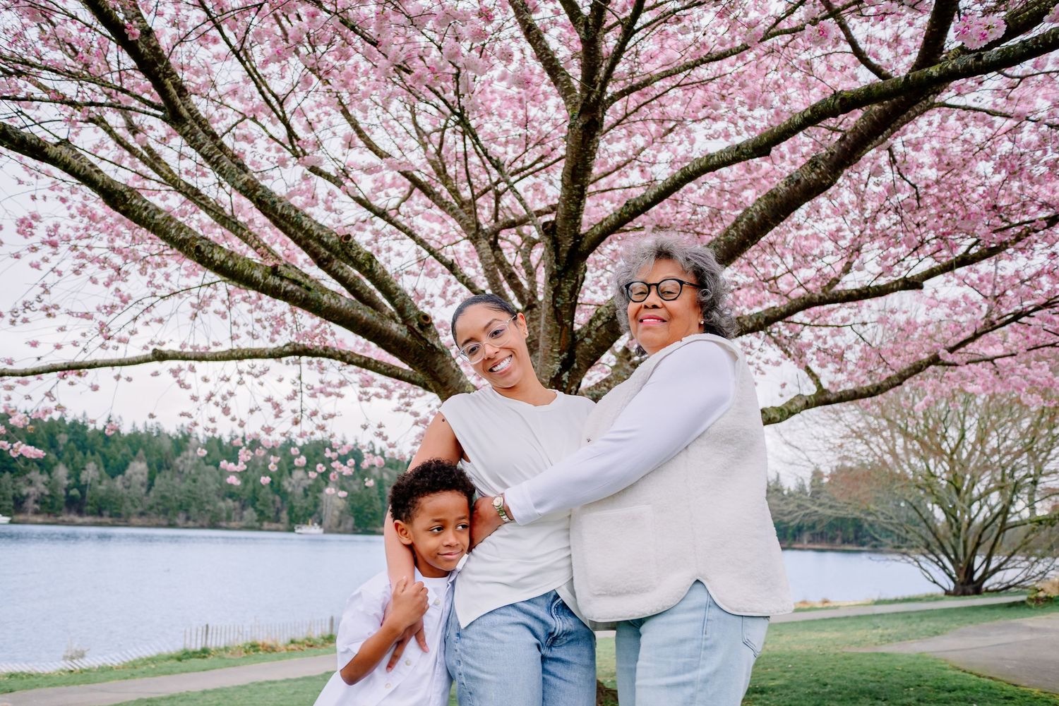 Multi-generational family smiling under cherry blossoms in Seattle beside Lake Washington. A grandmother, mother, and son family photo.
