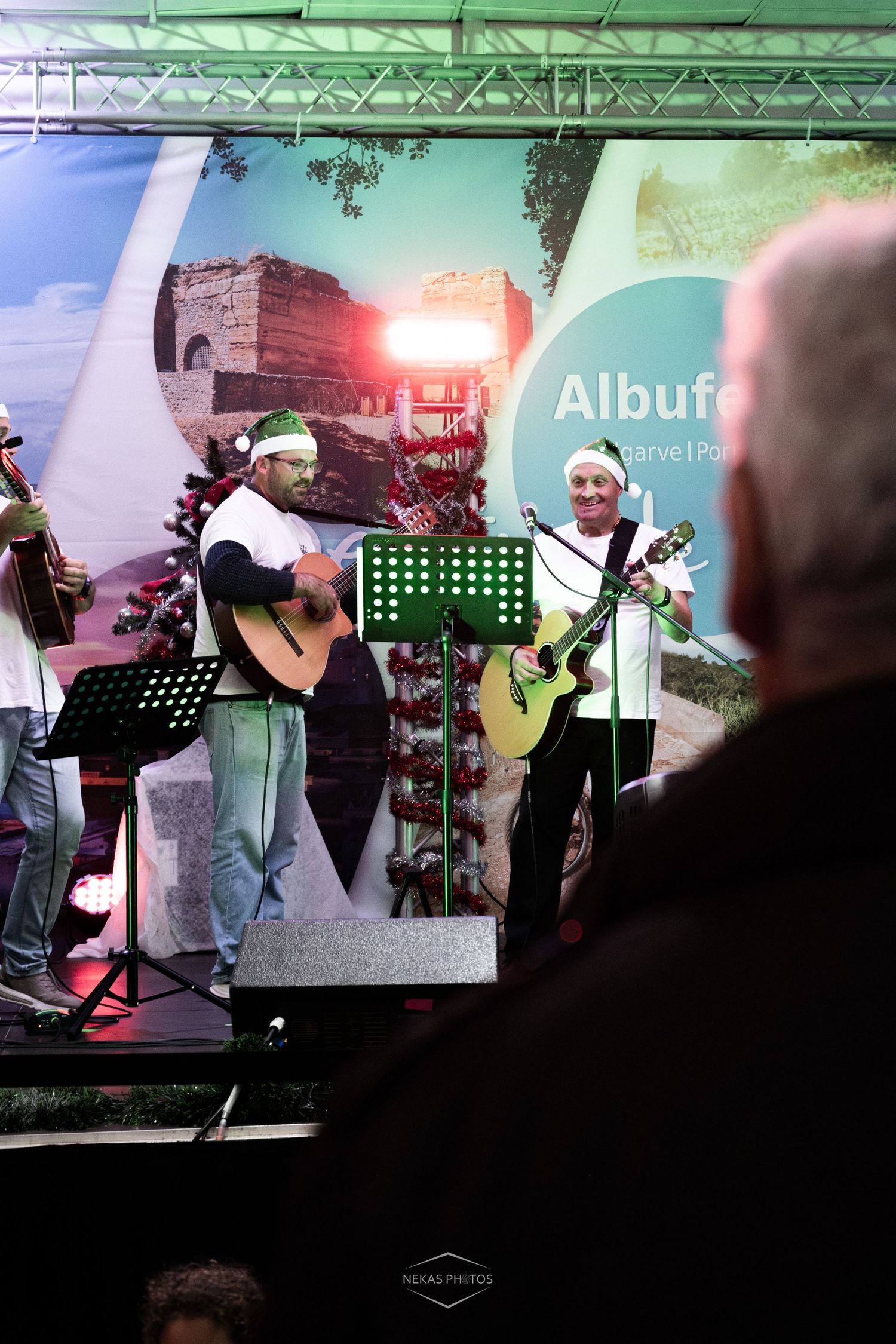 Musicians wearing Santa hats perform with guitars on stage at an Albufeira outdoor Christmas event in Portugal.