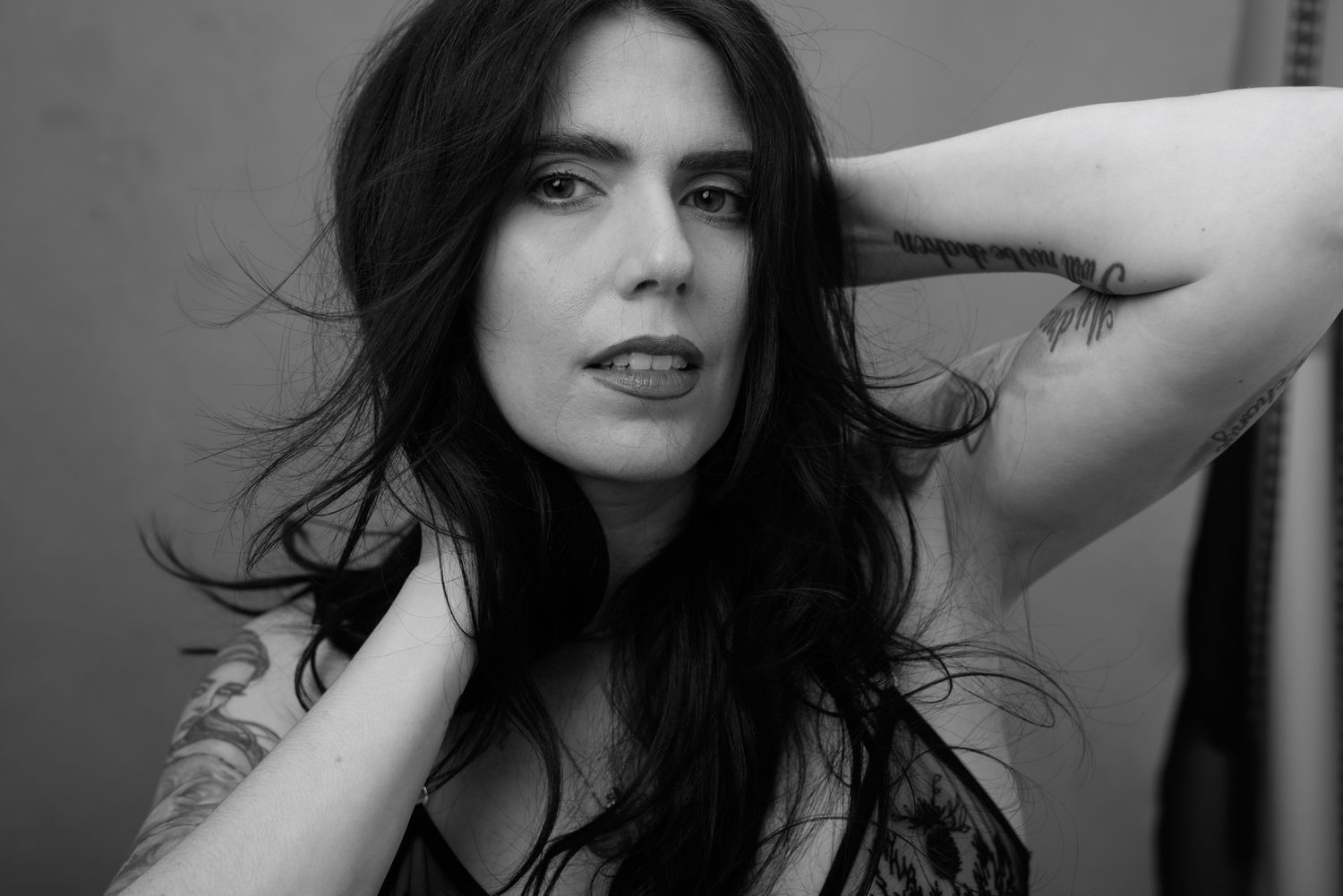 Black and white portrait of a woman with long dark hair wearing lace lingerie, posing confidently.