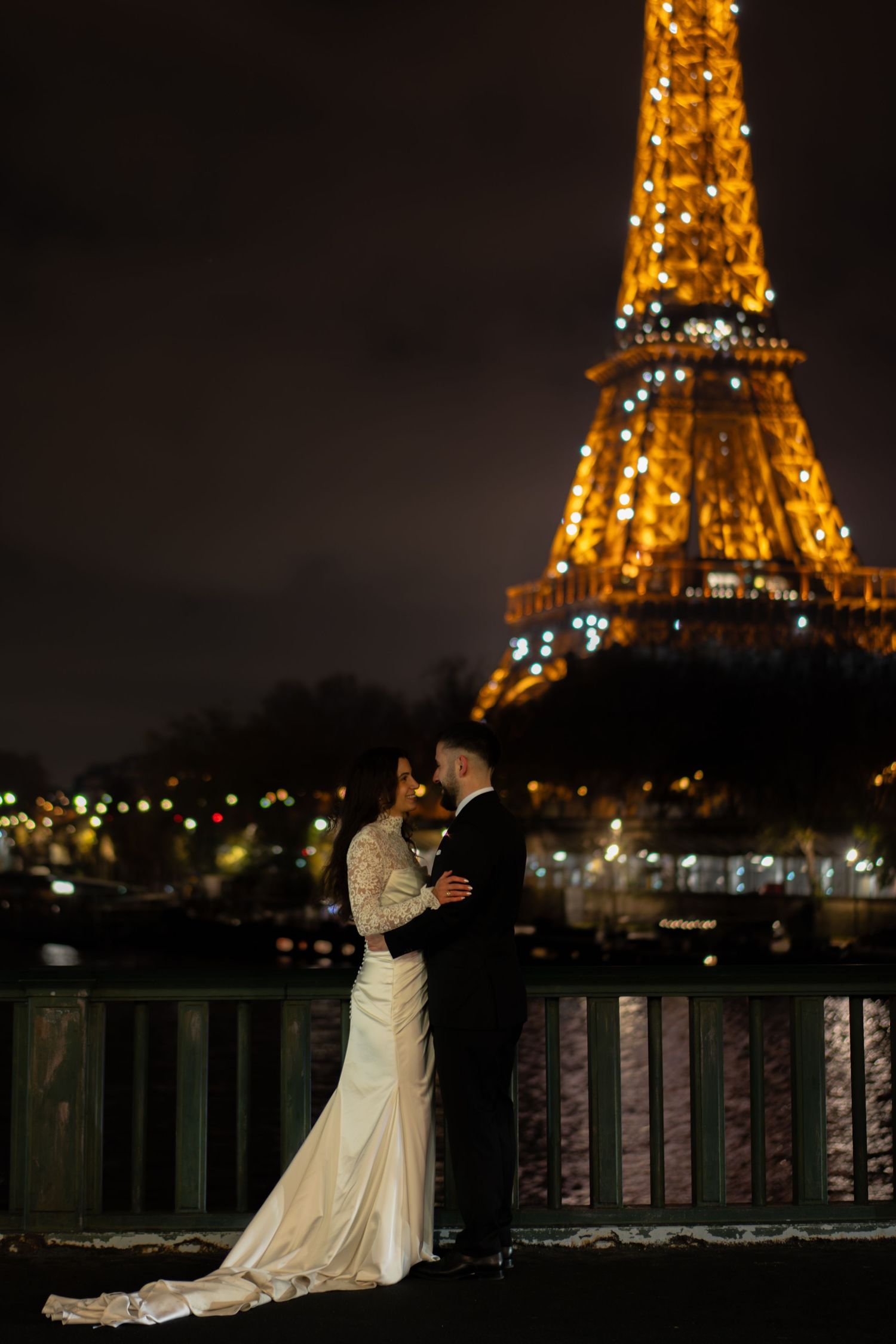 Bride and groom embrace in front of the illuminated Eiffel Tower at night in Paris. Paris film wedding photography