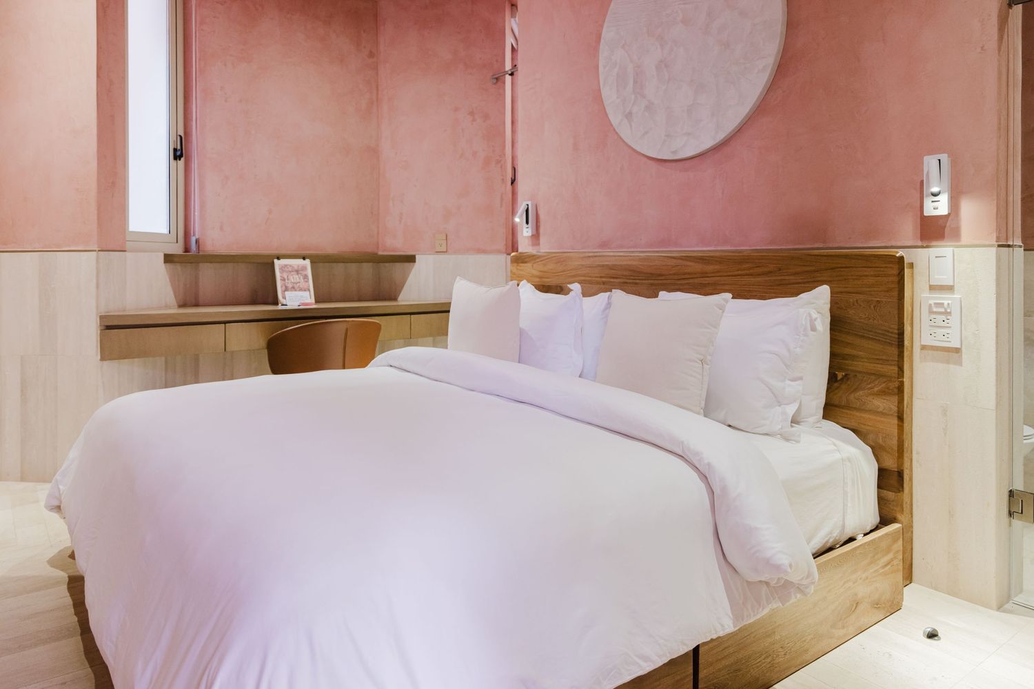 Cozy pink bedroom with a wooden bed frame, white bedding, and minimalist decor.