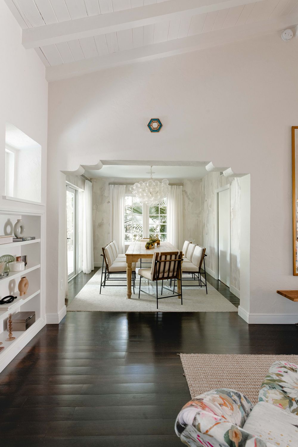 Bright dining room with wood table, upholstered chairs, bubble chandelier, dark hardwood floors, and white built-in shelving.