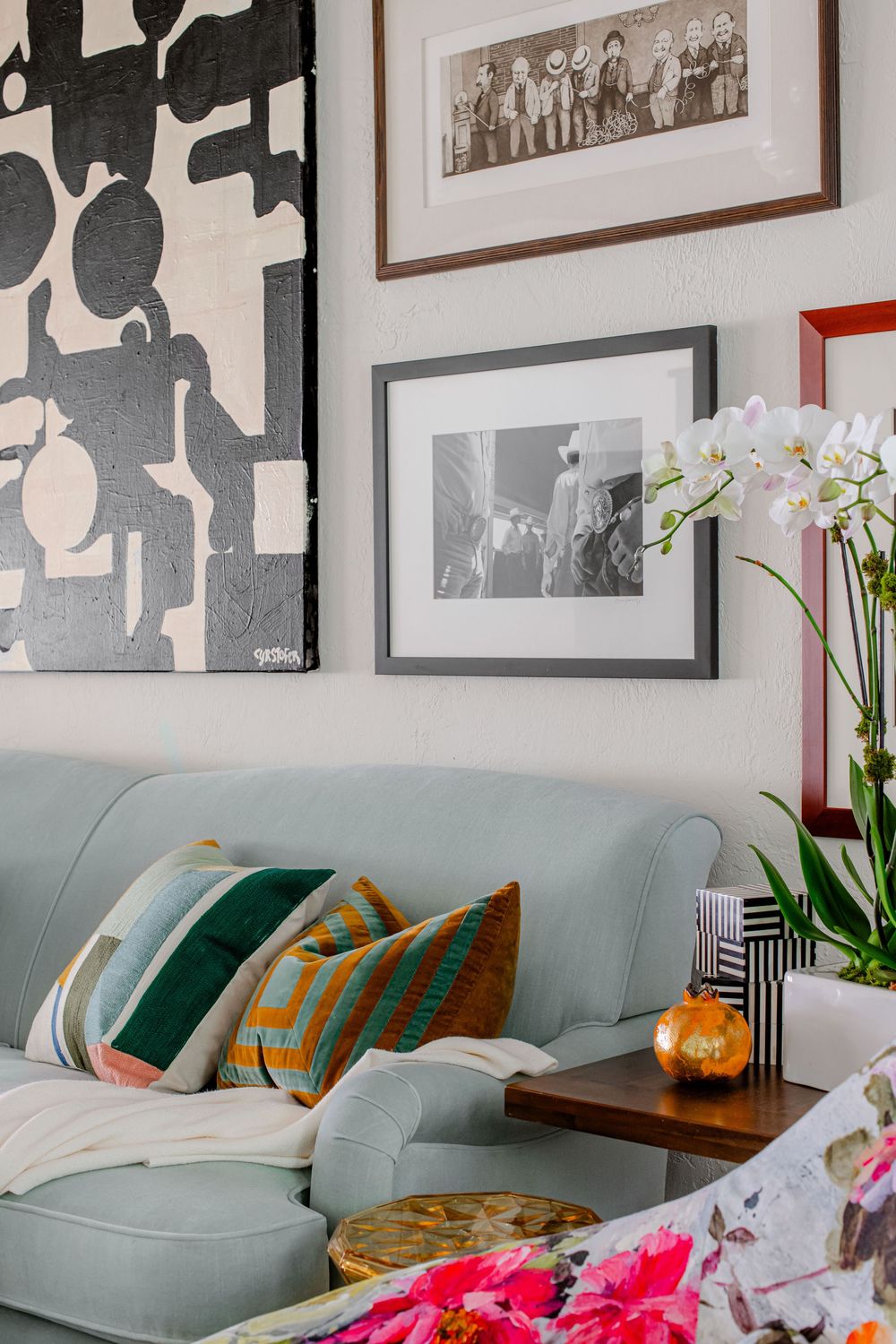 Light blue sofa with patterned pillows displayed beneath a gallery wall of black and white photos and abstract art.