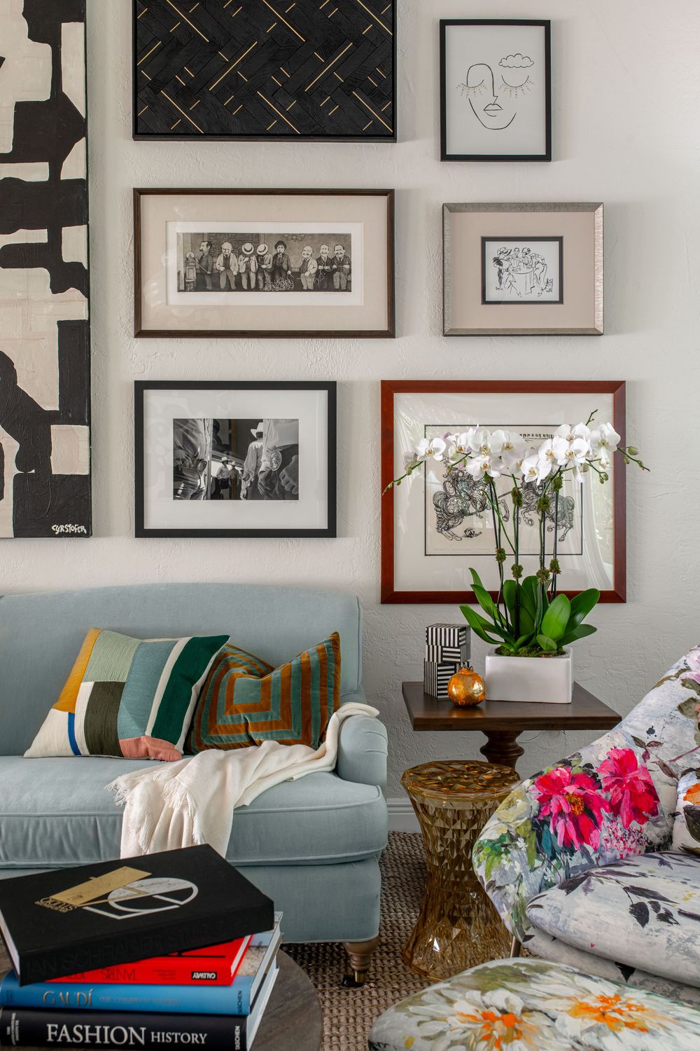 Cozy living room with blue sofa, floral chair, gallery wall of black and white art, orchid plant, and Fashion History coffee table books.