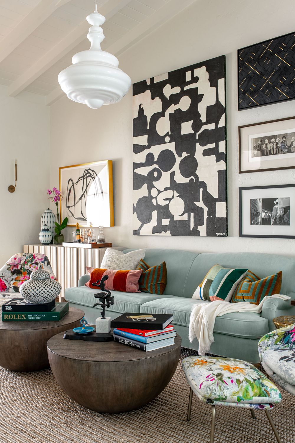 Eclectic living room with mint sofa, colorful pillows, bold black-and-white wall art, round coffee tables, and a white pendant light.
