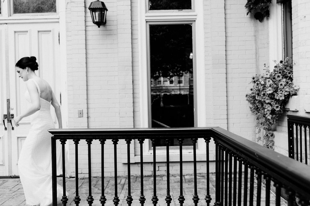 Black and white photo of a bride in a white gown standing on steps with iron railing outside The Fitzgerald venue.