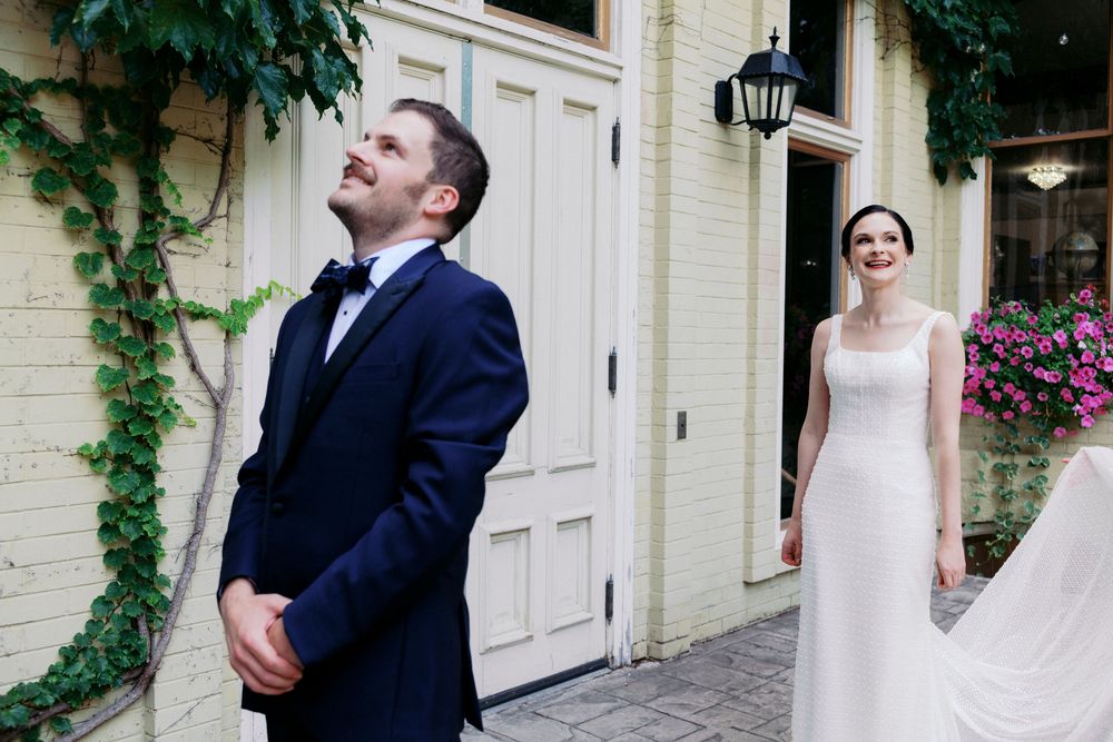 Midwest groom in navy suit reacts emotionally during first look with bride in white gown outside ivy-covered building.
