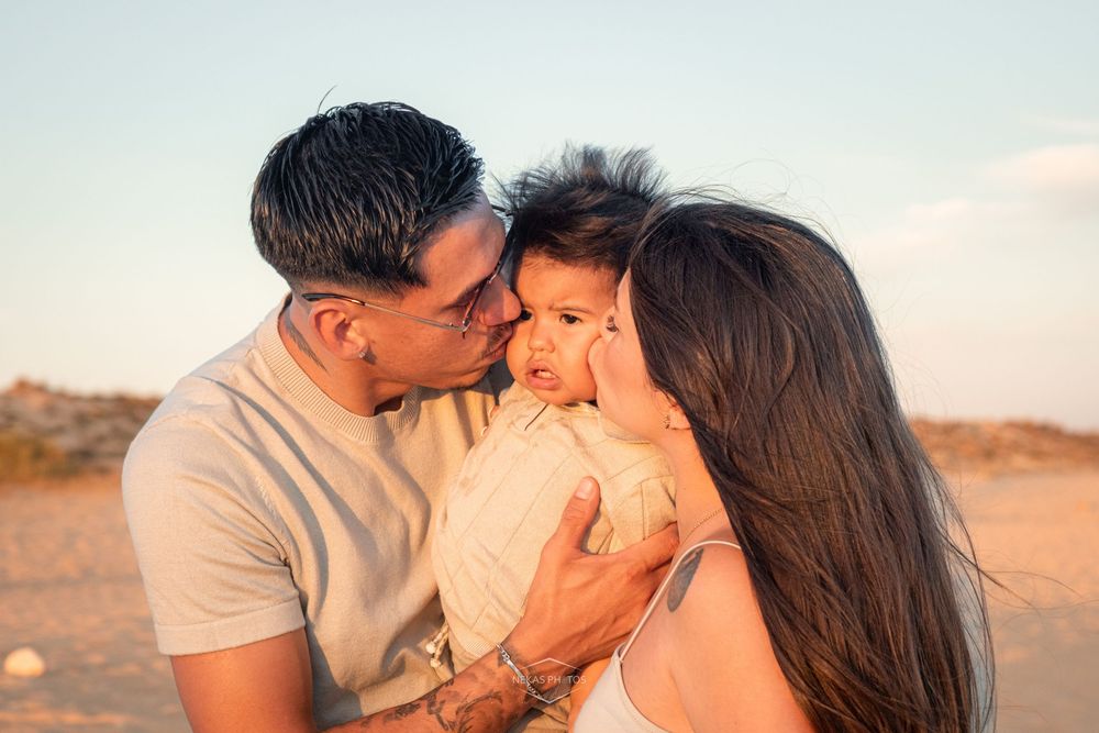 A loving family of three shares tender kisses on a sunny beach, parents embracing their toddler at golden hour.