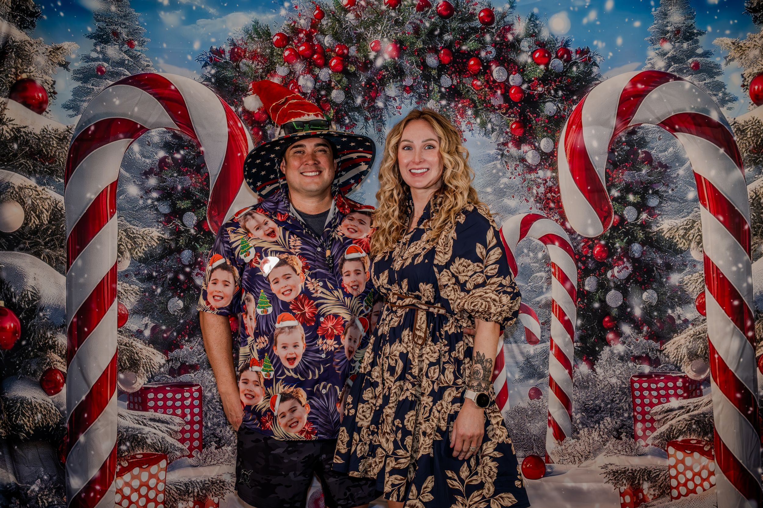 Couple posing in front of festive Christmas backdrop with candy canes and holiday decorations.