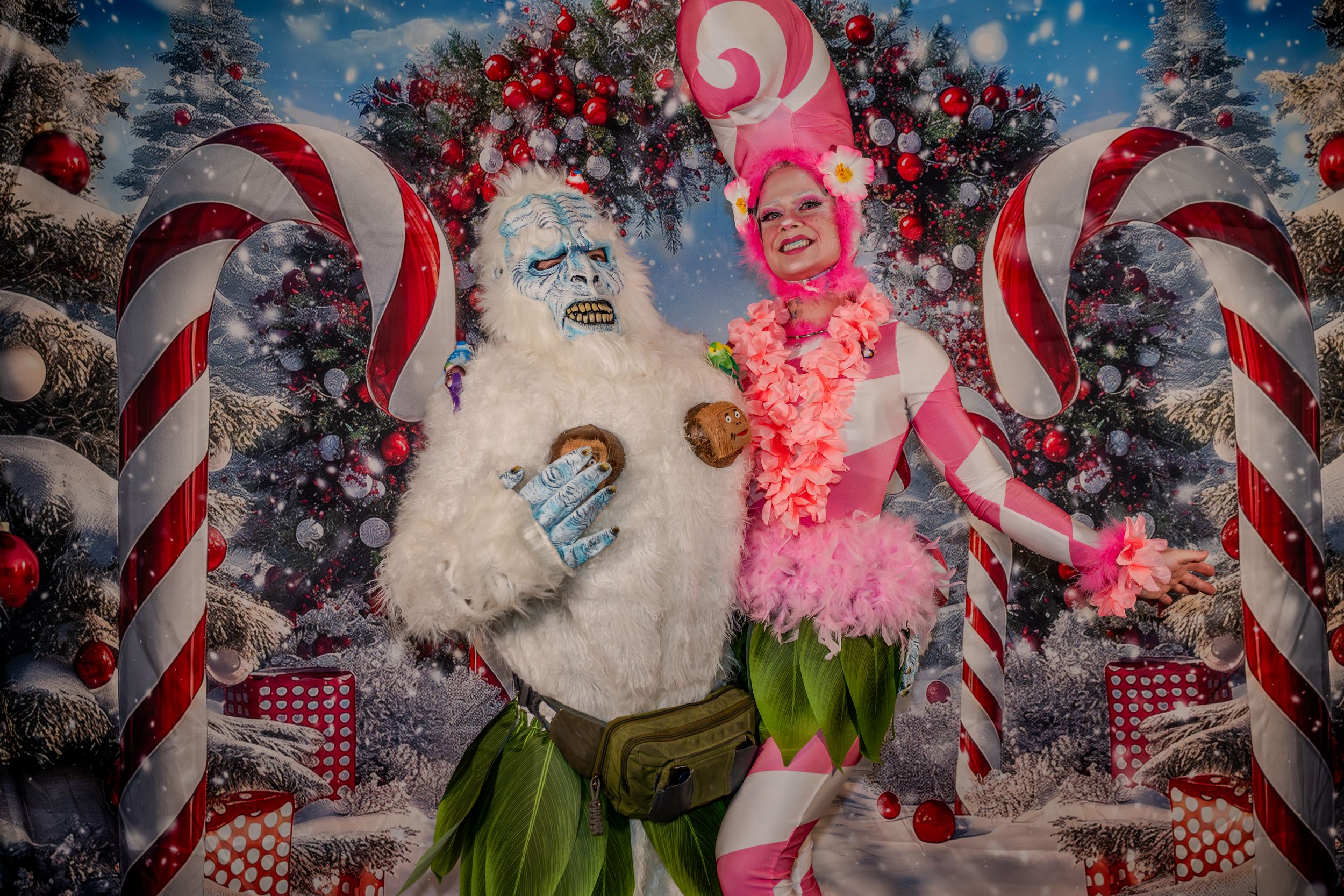 A yeti costume character and a pink festive performer pose in a colorful Christmas candy cane winter wonderland backdrop.