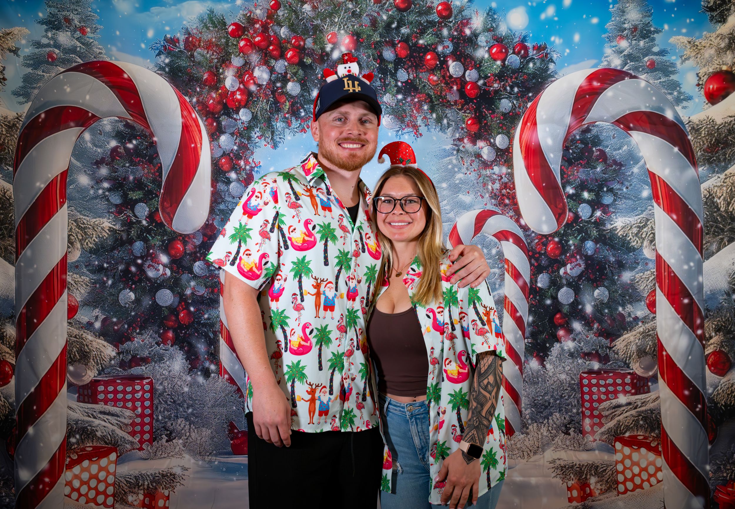 Couple smiling together in matching holiday shirts before a festive Christmas candy cane backdrop.