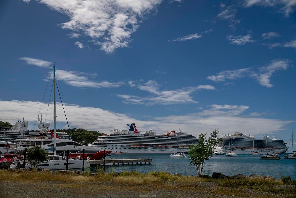 Large cruise ship docked at a tropical port marina with sailboats and blue sky with clouds in the background.