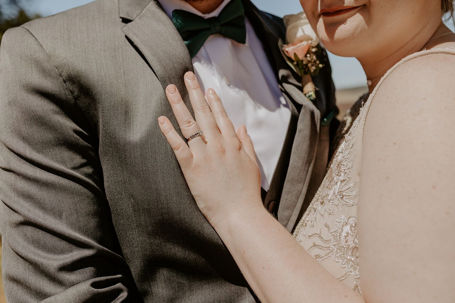 Bride placing hand on groom's chest showing wedding ring, groom in gray suit with green bow tie at Lake Cuyamaca, Julian.