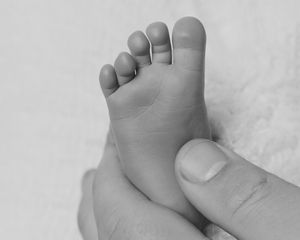 Close-up black and white photo of a tiny newborn baby foot cradled gently in an adult's hand.