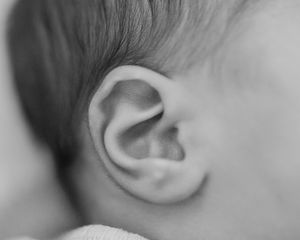 Close-up black and white photo of a newborn baby's ear, showcasing delicate skin and tiny features.