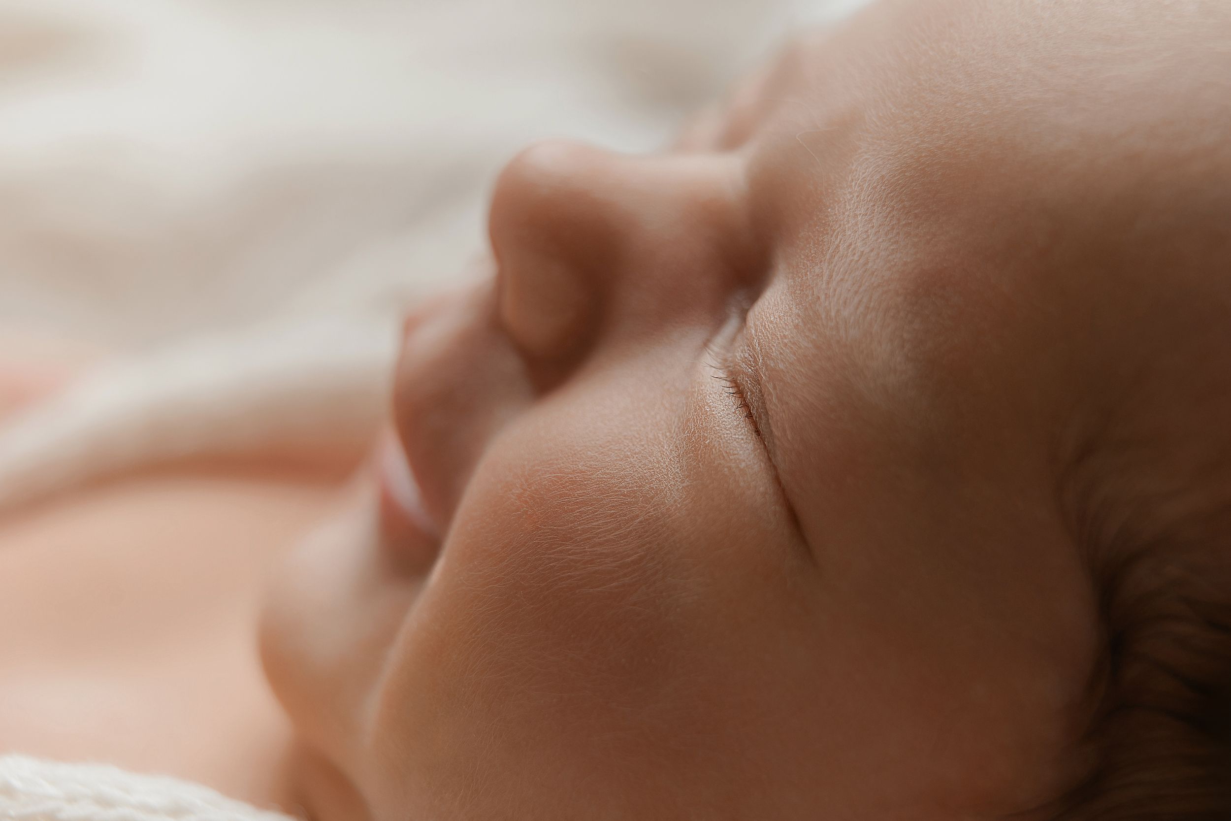 Close-up of a peaceful sleeping newborn baby with soft skin and delicate features resting on a light blanket.