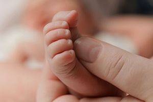 Close-up of a newborn baby's tiny feet being gently held by an adult's hand.