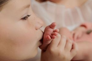 Young child tenderly kissing newborn baby's tiny feet in a close-up portrait photo.