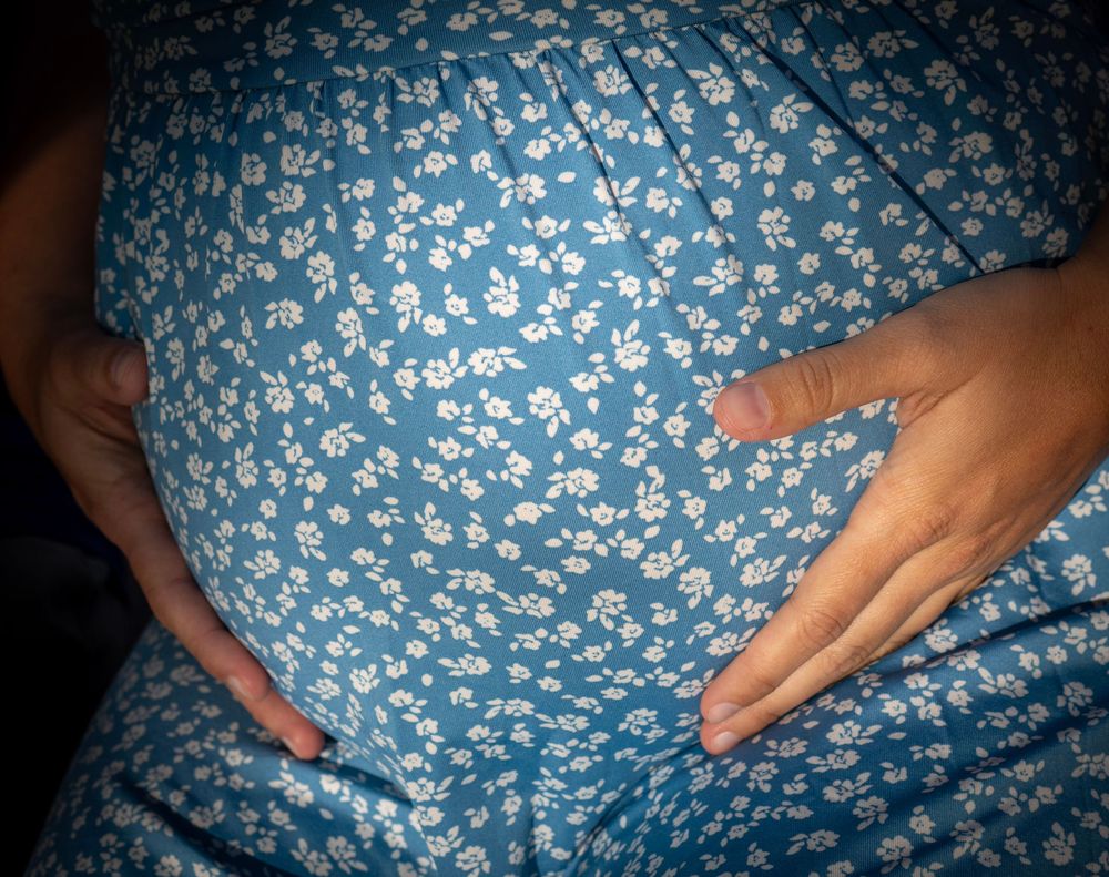 Pregnant woman in blue floral dress cradling baby bump with both hands.
