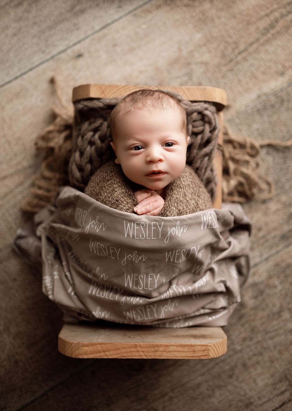 Newborn baby Wesley John wrapped in a personalized name blanket, nestled in a rustic wooden mini bed prop.