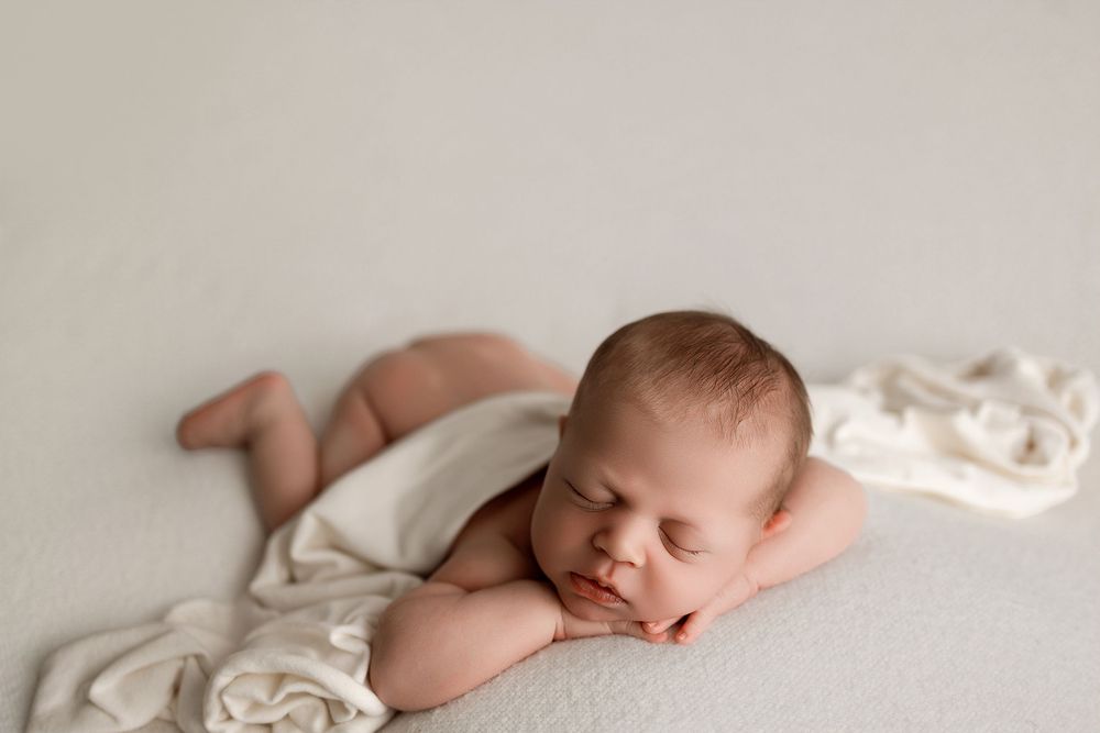 Newborn baby sleeping peacefully on a soft white blanket in a professional studio photography session.