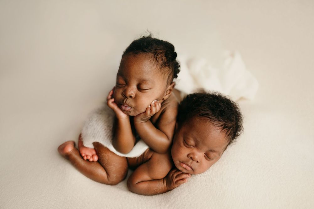 Two sleeping newborn twins posed together on a soft cream blanket in a professional newborn photography session.