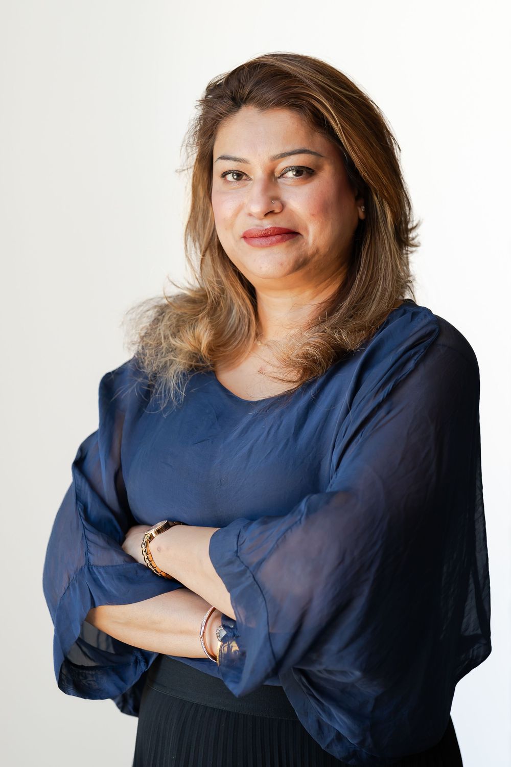 Professional woman in blue blouse with arms crossed, smiling confidently against white background.