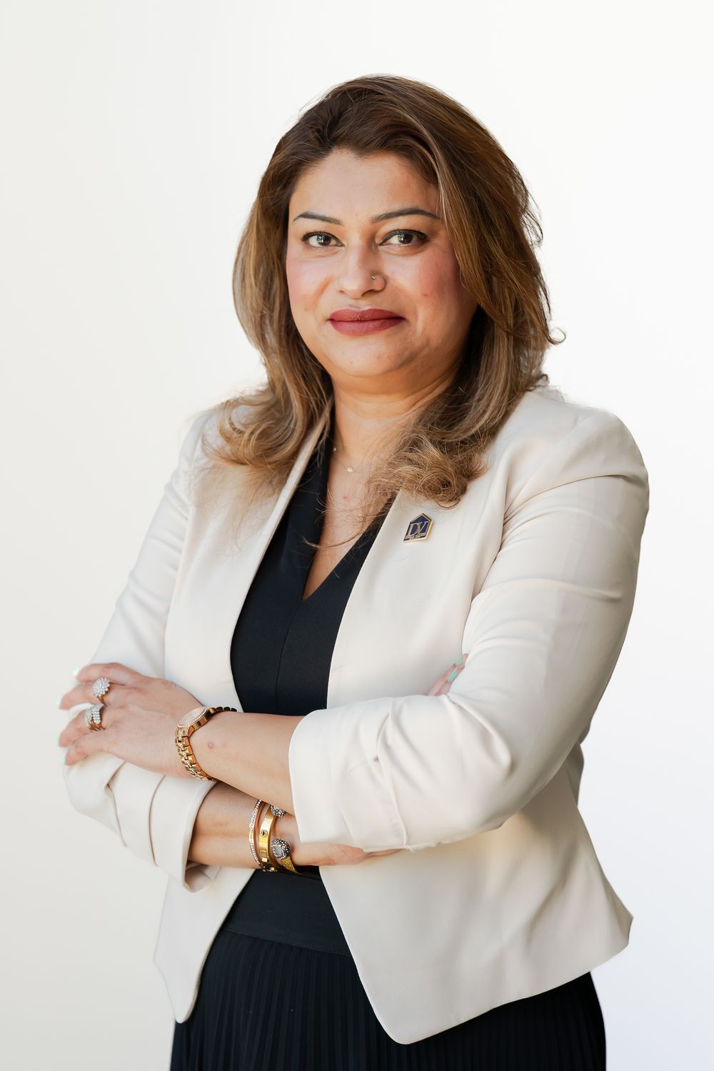 Professional woman in cream blazer and black top poses confidently with arms crossed against white background.