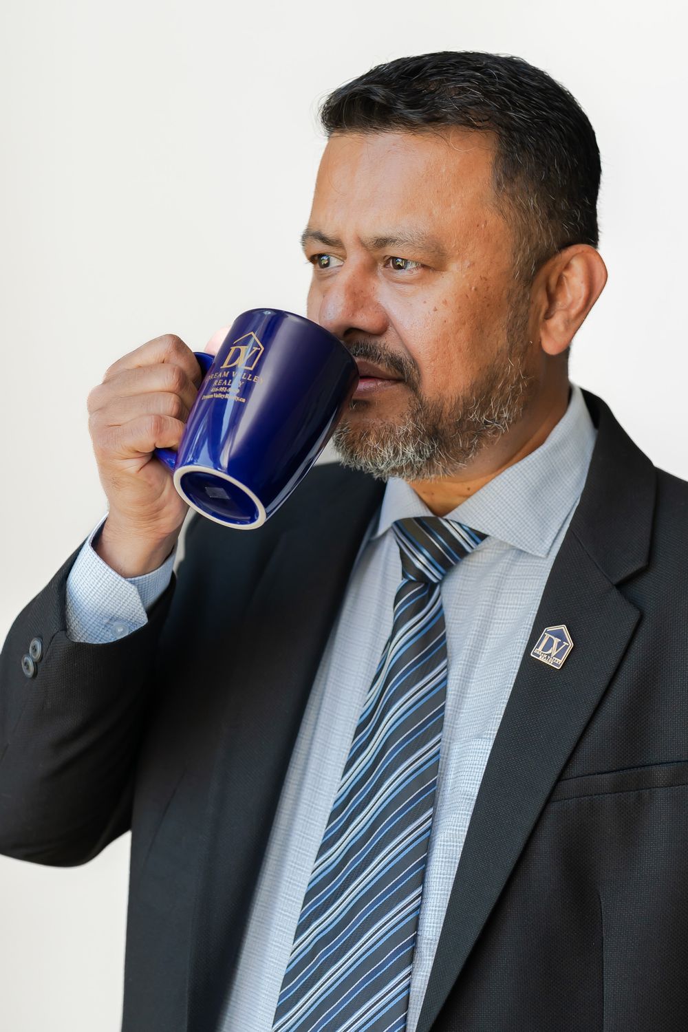 A professional businessman in a suit and tie drinking from a blue coffee mug against a white background.