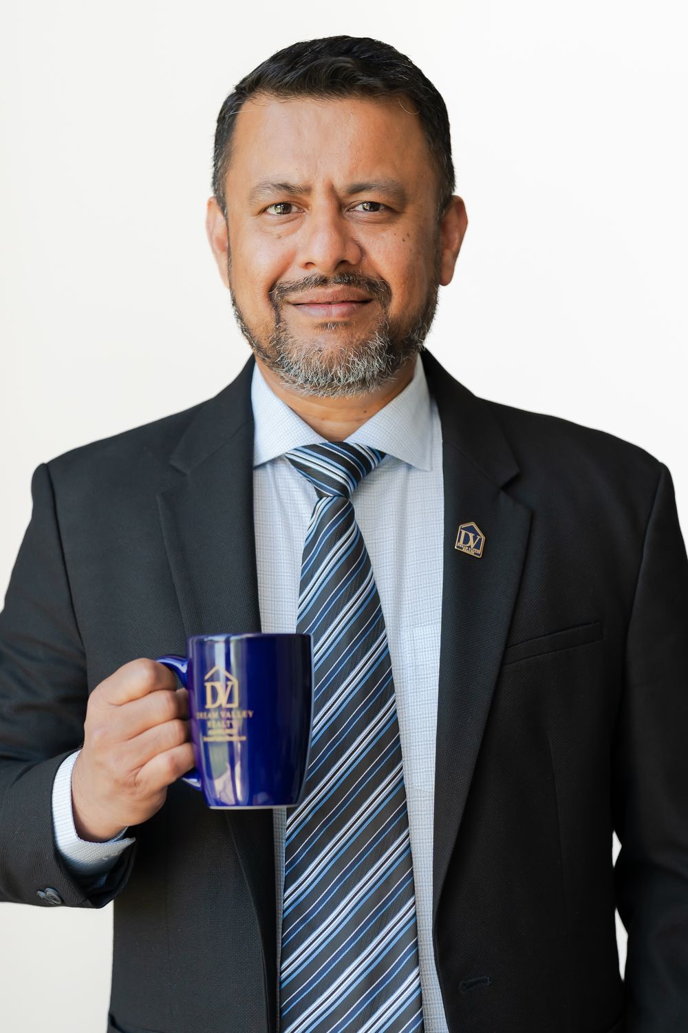 Professional man in suit and tie holding a blue branded mug, smiling confidently against a white background.