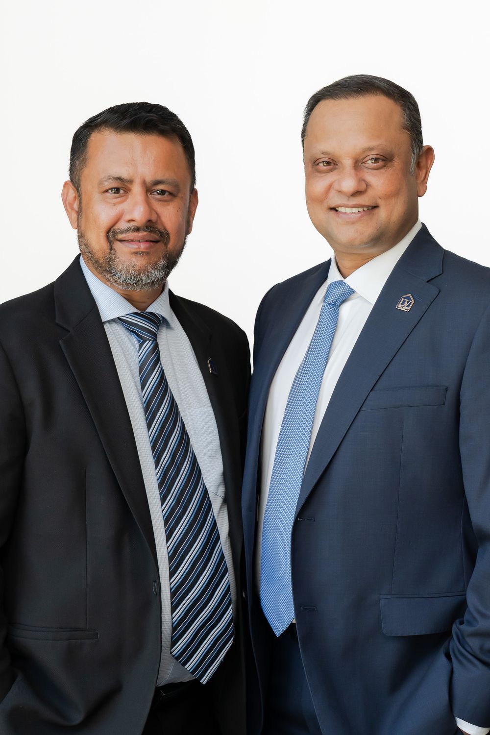 Two professionally dressed men in suits and ties smiling together against a white background.