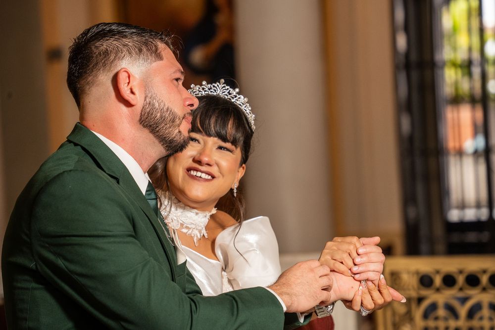 Bride wearing tiara and groom in green suit exchange rings during wedding ceremony indoors.
