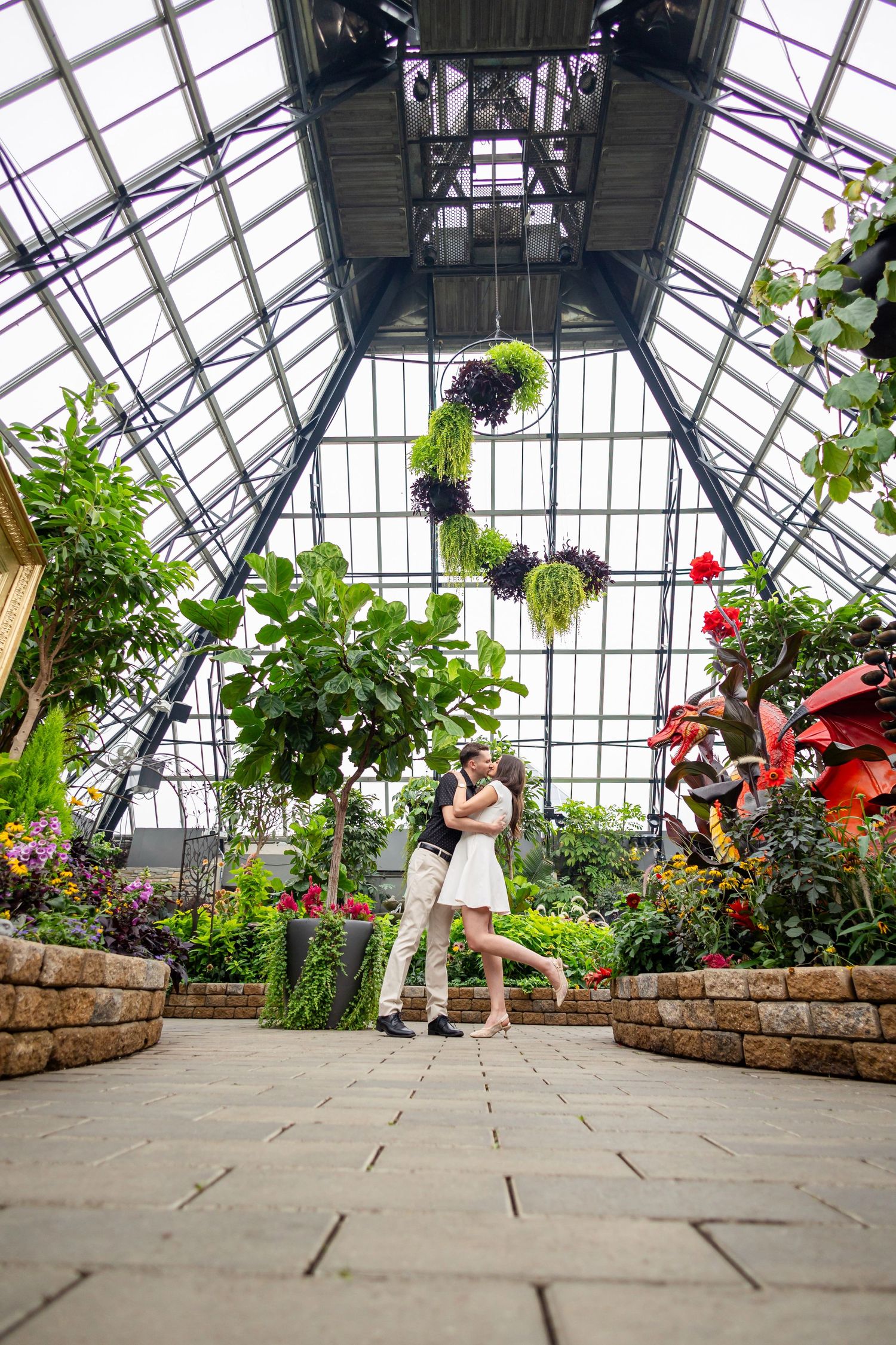 A romantic greenhouse photoshoot sequence showing a couple dancing among indoor garden planters and glass ceiling.