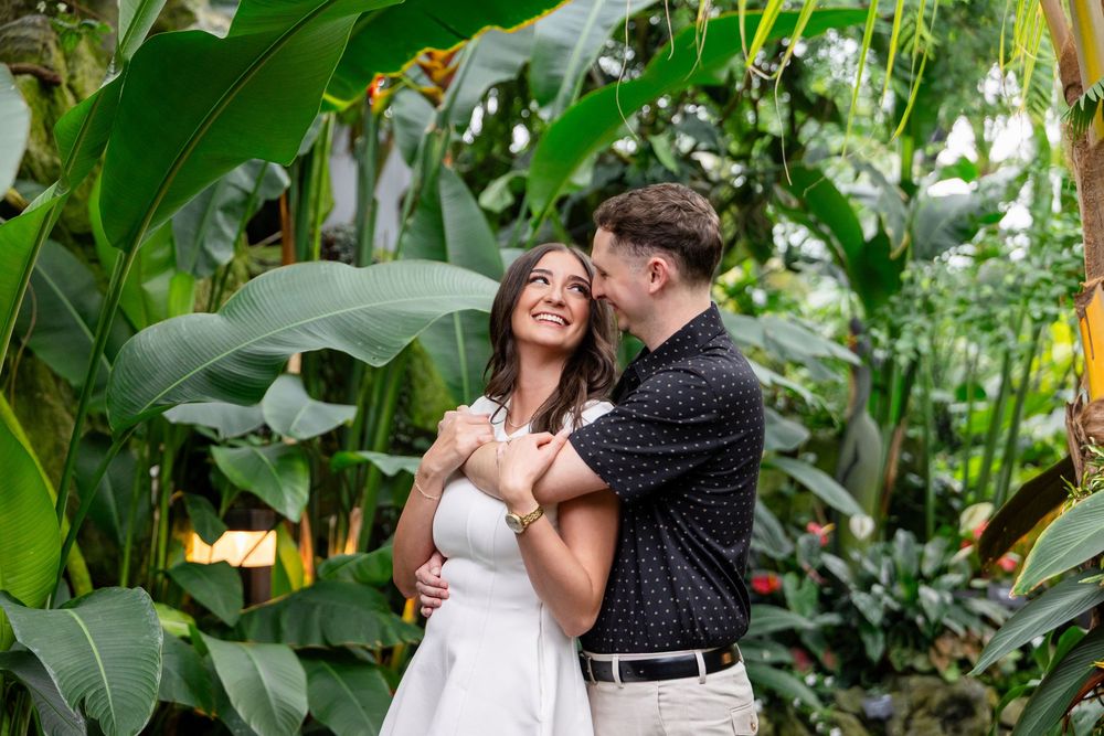A romantic couple shares a tender moment in a lush tropical garden setting with vibrant green foliage.